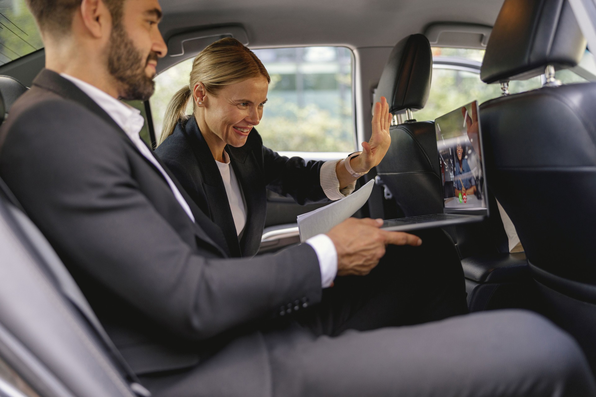 Cheerful business people have online meeting using laptop while sitting in car back seats